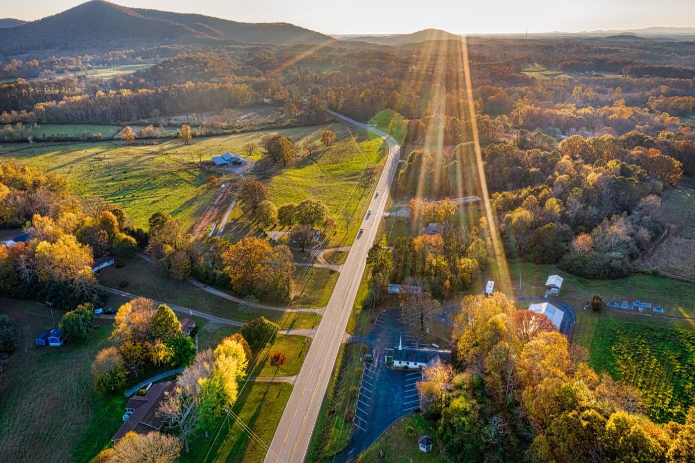 Aerial view of rural land at sunrise — open pasture, tree lines, and a country highway.
